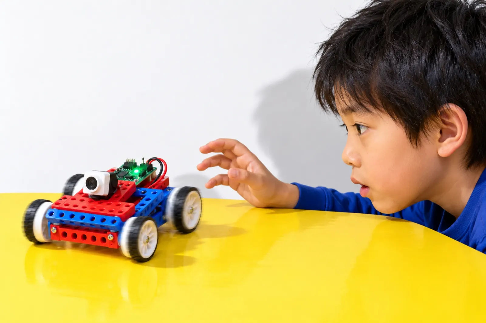 手を放したロボットが走りだすのを、机の高さで見つめる男の子の横顔（写真は見本）