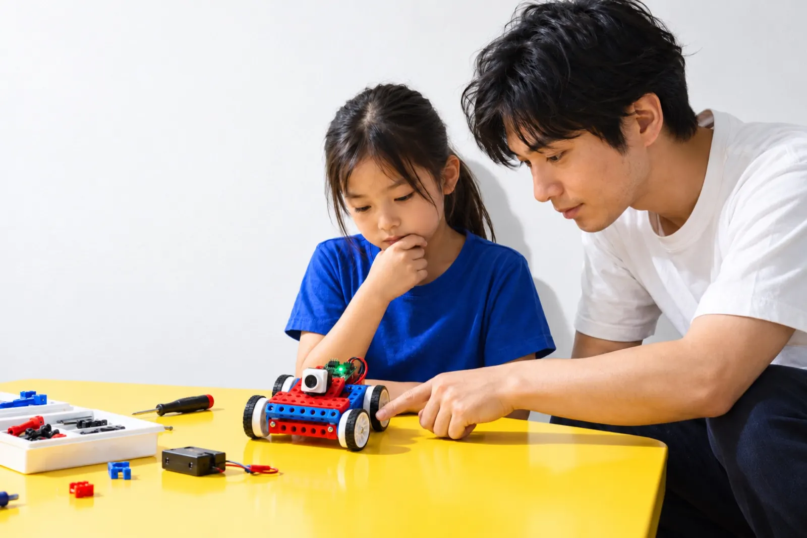 ロボットの車輪を指さす先生と、あごに手をあてて考える女の子（写真は見本）
